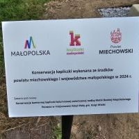 Tablica z logiem Wojew&oacute;dztwa Małopolskiego, Powiatu Miechowskiego oraz Kapliczki Małopolski informująca o źr&oacute;dłach finansowania